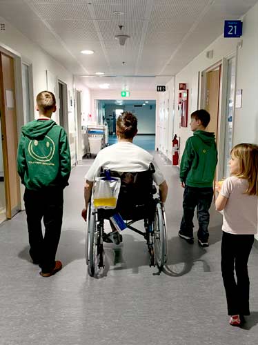 Familiefar i kørestol på hospitalet - omgivet af børn